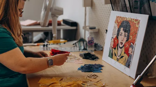 Image of the artist sitting at a table sorting fabric for a mosaic